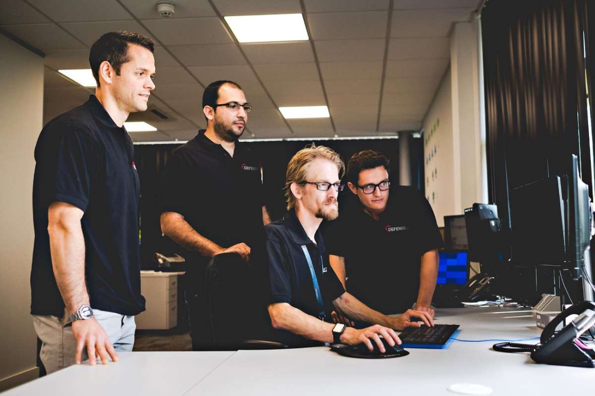 Defense.com SOC analysts gathered around a workstation
